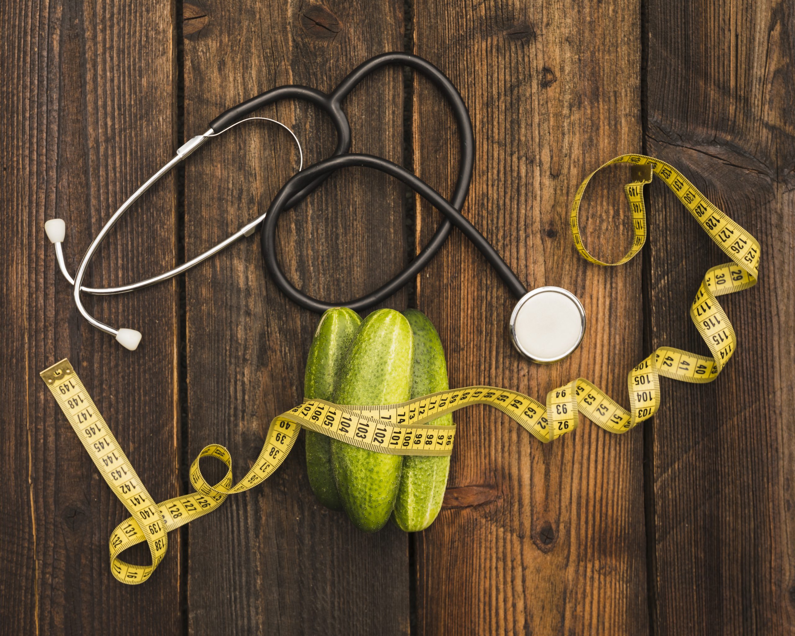 Measuring tape and stethoscope beside cucumbers, representing healthy weight loss through fasting