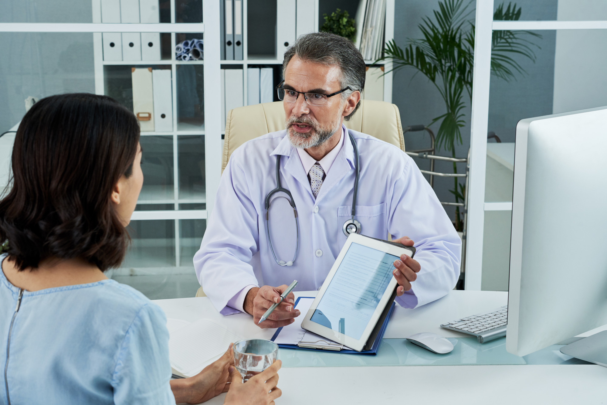 medium-shot-middle-aged-doctor-explaining-diagnosis-via-tablet-pc Doctor reviewing a patient's results and plan on a tablet
